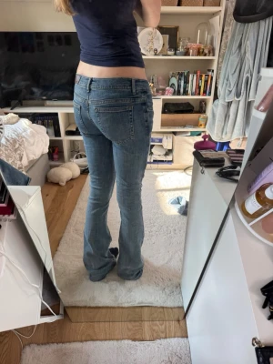 Blå bootcut jeans med låg midja - Säljer ett par klassiska blå bootcut jeans med låg midja och fem fickor. Jeansen har en lätt tvättad look och sitter tajt över låren för att sedan bli vidare nedtill. Perfekta för en avslappnad och trendig stil. Storlek xs! 
