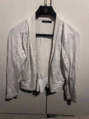 Vit öppen kofta med volangkant - Snygg vit kofta med öppen front och volangkant nedtill. Långärmad modell i mjukt och tunt material, perfekt att slänga över en topp. Enkel och stilren design som passar till det mesta. Går att få bort fläcken genom att tvätta.