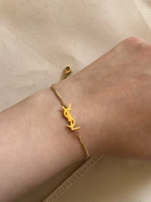 Guldigt armband  - Snyggt och stilrent armband i guldton  som detalj. Kedjan är tunn och smidig med ett diskret lås och en liten bricka. Perfekt accessoar för att lyfta din outfit.