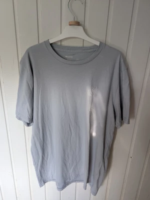 Ljusgrå t-shirt från Hollister - En stilren ljusgrå t-shirt från Hollister i Core Fit-modell. Tillverkad i 100% bomull för en mjuk och bekväm känsla. Klassisk rund halsringning och korta ärmar, perfekt till alla outfits.