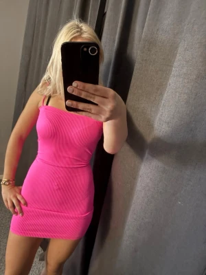 Rosa ribbad kortklänning Dunnes - Säljer en snygg ribbad kortklänning från Dunnes i stark rosa färg. Klänningen är axelbandslös och har en tight passform som framhäver figuren. Perfekt för dig som vill sticka ut med en färgglad och trendig look.