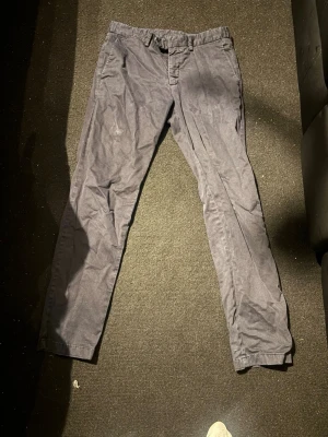 Oscar Jacobsson kostymbyxor/chinos - Snygga mörkblå chinos med smal passform och klassisk design. Byxorna har framfickor, bälteshällor och stängs med knapp och dragkedja. Perfekta för dig som vill ha en stilren och enkel look. Materialet känns mjukt och bekvämt.