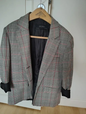 Rutig kavaj från Zara Basic - Snygg rutig kavaj från Zara Basic Collection med klassiskt svartvitt hundtandsmönster och tunna röda ränder. Kavajen har breda slag, två framfickor och svart innerfoder. 