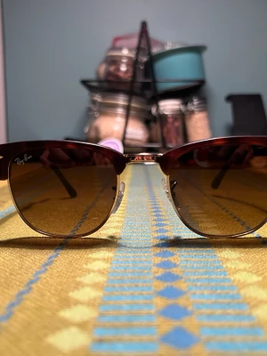 Ray-Ban bruna clubmaster solglasögon - Säljer ett par klassiska Ray-Ban clubmaster solglasögon med bruna bågar och guldfärgade detaljer. Glasen är tonade i brunt och bågarna har en retroinspirerad form. Perfekta för dig som vill ha en tidlös och cool look.
