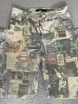 Street art-printade jeans Jaded London - Unika jeans från Jaded London med all-over street art och collage-print i beige, grå och svarta toner. Rak passform och jeansen är supercoola. 