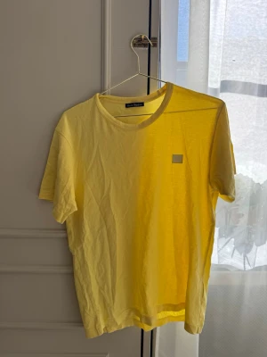 Gul t-shirt från Acne Studios - Snygg gul t-shirt från Acne Studios med klassisk rund hals och korta ärmar. Tillverkad i mjukt bomullsmaterial och har den ikoniska Acne Studios-loggan på bröstet. Perfekt för en avslappnad och trendig look.