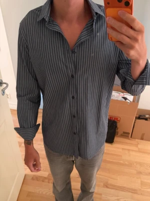 Mörkblå randig skjorta med knappar - Säljer en mörkgrå skjorta från Massimo dutti den är helt ny och aldrig använd, size skulle jag säga är mellan m/l beroende hur man vill att den ska sitta.