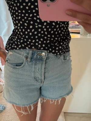 Ljusblå jeansshorts med fransig kant - Säljer ett par ljusblå jeansshorts med rå, fransig kant och klassisk femficksmodell. Shortsen har normal passform och är perfekta för varma dagar. Perfekta ljusblåa färgen för att kunna styla med fina toppar,blusar eller stickade tröjor🩷