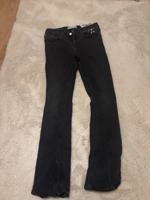 Svarta bootcut lågmidjade jeans från Calvin Klein - Säljer ett par svarta bootcut jeans från Calvin Klein med klassisk femficksmodell och logga på fickan. Jeansen har normal lågmidjade och raka ben med lätt utsvängning. Perfekta för en avslappnad men ändå snygg look. Storleken är för 16 åringar men funkar för dig som har xs/s💕