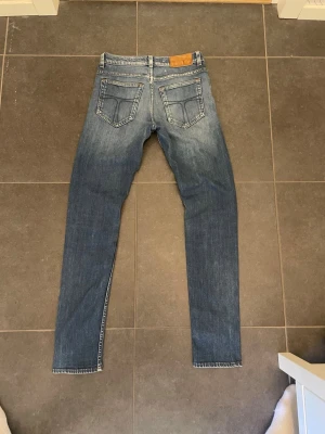 Tiger of Sweden blå slim fit jeans  - Snygga blå slim fit jeans med ljusa slitningar på lår och knän.  normalhög midja och raka ben. Jeansen är Perfekta för en trendig look.  Storlek 29/34 så det är ganska smala i midjan och långa i benen 