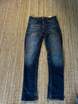 Mörkblå tapered jeans Jack & Jones - Snygga mörkblå jeans från Jack & Jones med tapered fit och klassisk femficksmodell. Jeansen har en lätt tvättad look med subtila slitningar och raka ben. Perfekta för dig som gillar en avslappnad men ändå stilren stil. ❗️w28 L32❗️