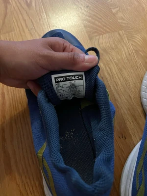 Blå sneakers från Pro Touch - Snygga blå sneakers från Pro Touch med vita och svarta sulor samt gula detaljer på sidan. Ovandelen är i mesh-tyg för bra andningsförmåga och skon har klassisk snörning. Perfekta för dig som gillar sportig stil.