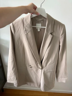 Beige kavaj från H&M - Stilren beige kavaj från H&M. Något större i storleken. Använd enstaka gånger. 