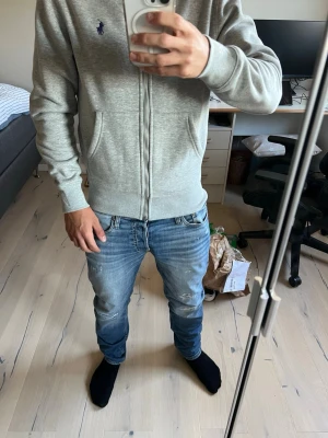 Grå polo Ralph lauren zip med huva  - Helt ny polo Ralph lauren zip i grå färg, tog bilder på de fina detaljerna som de flesta inte har på sina Ralph lauren zips, ingen, slitage, missfärgning eller hål finns. Hör gärna av er om ni blir intresserade. Kan även skicka fler bilder på den, hoodien passar även någon som är runt 166 cm lång