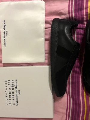 Maison Margiela svarta sneakers - Svarta sneakers från Maison Margiela i stilren design. Tillverkade i en mix av läder och mocka med ton-i-ton detaljer och klassisk gummisula. Perfekta för dig som gillar minimalistisk och clean stil. Vid snabbaffär 