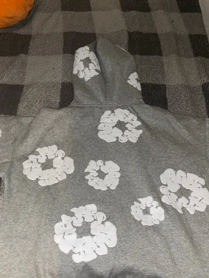 Grå hoodie med vita blommor - Denim Tears Cotton Wreath Hoodie – M / passar L–XL  Säljer en grå Denim Tears Cotton Wreath Hoodie med det ikoniska vita wreath-trycket.  • Storlek: M enligt etiketten • Passar även L–XL tack vare oversized passform • Färg: Grå/vit • Skick: Oanvänd / mycket fint skick • Tags kvar • Mjukt och tjockare material • Känguruficka framtill  Riktigt snygg och eftertraktad modell. Säljer då den inte kommer till användning.  Pris: 800 kr, kan diskuteras vid snabb affär.