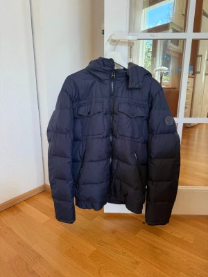 Mörkblå dunjacka från Marc O'Polo - Snygg mörkblå dunjacka från Marc O'Polo med huva och dragkedja framtill. Jackan är varsamt använd och i väldigt bra skick!!🤩 passar perfekt för kallare dagar! 
