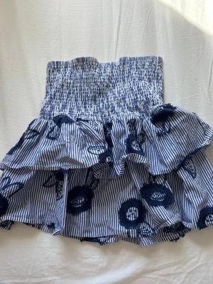 Blåvit volangkjol  - Supersöt blåvit kjol från Holly & Whyte by Lindex med smock i midjan och volanger. Kjolen har tunna ränder och broderade blommor i mörkblått. Kan användas som topp också! Storlek S. Knappt använd. Orginalpris 499.