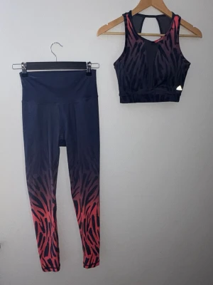 Adidas träningsset med mönster - Snyggt träningsset med topp och tights. Toppen har hål i ryggen och detaljer i mesh både fram och baktill. Materialet är stretchigt och passar perfekt för gym eller yoga. Storlek S men passar mer XS. 