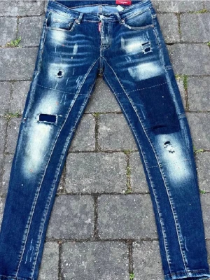 Dsquared2 - Säljer ett par blå jeans från Dsquared2 med slitna detaljer, patchar och hål för en riktigt edgy look. Jeansen har skinny fit, klassiska fem fickor och coola kontrastsömmar. Perfekta för dig som gillar streetstyle och vill sticka ut.