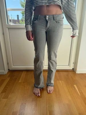 Ljusgrå raka jeans med låg midja - Säljer ett par ljusgrå jeans med rak passform och låg midja. Jeansen har klassiska fem fickor och stängs med knapp och dragkedja. Materialet är denim i bomull. Perfekta för en avslappnad och trendig look.
