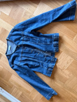 Klassisk blå jeansjacka - Snygg blå jeansjacka i klassisk modell med raka sömmar och långa ärmar. Jackan har knappstängning framtill och två dekorativa sömmar längs framsidan. Perfekt att slänga över en hoodie eller t-shirt för en avslappnad look.