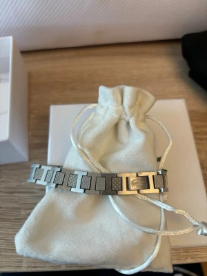 Lacoste armband - Snyggt armband från Lacoste i silverfärgad metall med rektangulära länkar och diskreta mönster på varje länk. Armbandet har en modern och minimalistisk design som passar till många olika stilar. Perfekt accessoar för dig som gillar stilrena detaljer.