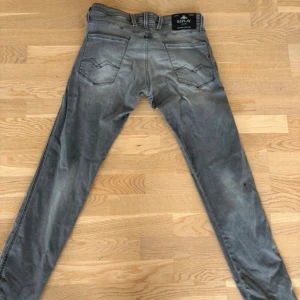 Replay anbass - Snygga grå slim fit jeans med lätt slitna detaljer och klassisk femficksdesign. Jeansen har normal midja och smala ben, perfekta för en avslappnad men trendig look. Materialet är denim med stretch för extra komfort.