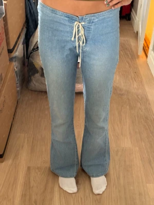 Ljusblå bootcut jeans med snörning - Säljer ett par ljusblå bootcut jeans med snörning i midjan. Jeansen har låg midja och är tillverkade i klassisk denim. Skulle säga storlek S/M, köpta second hand så finns ingen lapp på. Jag är 180 cm lång.