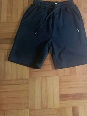 Mörkblå shorts från Polo Ralph Lauren - Snygga mörkblå shorts från Polo Ralph Lauren med klassisk broderad logga på benet. Shortsen har elastisk midja med snörning och är perfekta för sommardagar. Tillverkade i mjukt material för maximal komfort.