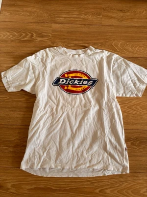 Vit Dickies t-shirt med logga - Vit t-shirt från Dickies med stor färgglad logga på bröstet. Klassisk passform och rund halsringning. Perfekt till jeans eller shorts för en avslappnad streetwear-look.