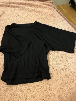 Svart loose-fit t-shirt - En svart t-shirt i loose-fit modell med korta ärmar och rund hals. Tillverkad i mjukt bomullstyg som känns skönt mot huden. Perfekt för en avslappnad och enkel stil. Passar till det mesta och är lätt att matcha med andra plagg.