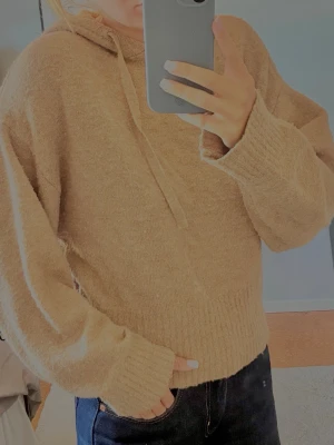 Beige fluffig hoodie med huva - Mysig beige hoodie i fluffigt material med huva och dragsnören. Tröjan har avslappnad passform, långa ärmar och breda ribbade muddar vid ärmslut och nederkant. Perfekt för chill dagar och enkel att matcha med jeans eller leggings.