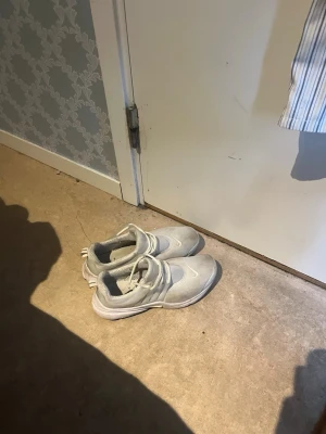 Nike Presto - Säljer ett par vita sneakers med klassisk design och snörning. Skorna har en rund tå och tjock sula, vilket ger en sportig look. Materialet ser ut att vara en mix av textil och syntet. Perfekta för dig som gillar stilrena och bekväma skor.