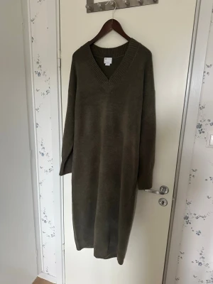 Olivgrön stickad långklänning ASOS - Mysig olivgrön stickad långklänning från ASOS med v-ringad hals och långa ärmar. Klänningen har en relaxed passform och bred ribbad kant vid halsen. Perfekt för kyligare dagar och enkel att styla med boots eller sneakers. Storlek L/40. Jag upplevde den som lite större i modellen, så den kan även passa XL beroende på önskad passform. Använd en gång. Det är lite “see through” vid sömmarna på axlarna, men enligt mig syns det främst på insidan vid axlarna. Katt finns i hemmet 