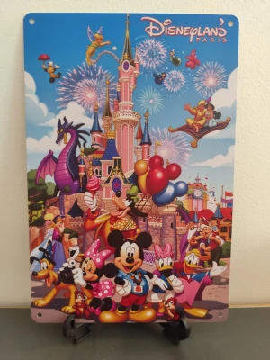 Disneyland Paris metallskylt - Färgglad metallskylt med motiv från Disneyland Paris. Skylten visar klassiska Disneyfigurer som Musse Pigg, Mimmi, Kalle Anka och Långben framför slottet, med ballonger, fyrverkerier och sagokaraktärer i bakgrunden. Perfekt som dekoration för Disneyfans.