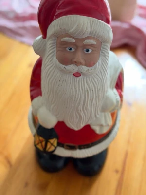 Dekorativ tomtefigur med lykta - Säljer en stor tomtefigur i keramik , med klassisk röd tomtedräkt, vitt skägg och svart bälte. Tomten håller en svart och gul lykta i ena handen. Perfekt som juldekoration för att skapa mysig stämning hemma. Tomten är 35 cm hög och 25 cm bred.