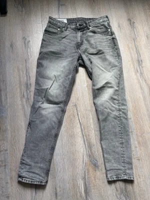 Grå taperd fit jeans - Säljer ett par grå taperd fit jeans med klassisk femficksmodell och dragkedjegylf. Jeansen har en tvättad look och raka ben. Perfekta till en avslappnad stil och passar till det mesta i garderoben.