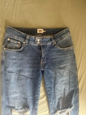 Blå slitna jeans från 157 - Ett par blå jeans från 157 med slitningar vid knäna