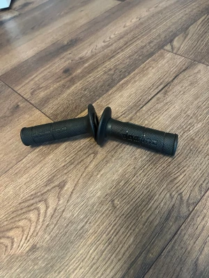 Svarta domino handtag till moped - Säljer ett par svarta handtag i gummi med räfflad yta och skyddande fläns. Passar till cykel och moppe. Greppen har ett mönster för bättre grepp och är enkla att montera på styret.