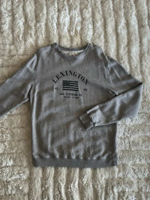 Lexington sweatshirt i grå - stl L - Lexington sweatshirt i grå, storlek L. Mjuk bomull med lite tvättad yta, rak passform. Personen på bilden är 189cm, väger 78kg.  Använd men i mycket fint skick, inga hål eller fläckar.  Rök- och djurfritt hem. Skriv gärna om du vill ha fler bilder eller undrar något!