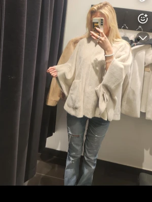 Ljusbeige ponchokappa med fickor - Säljer en supermjuk och fluffig ljusbeige ponchokappa med vida ärmar och två stora fickor framtill. Kappan har en avslappnad passform och är perfekt för lager på lager. Materialet känns lyxigt och ger en mysig vibe. Passar dig som vill ha något både trendigt och bekvämt. Nypris 1300kr