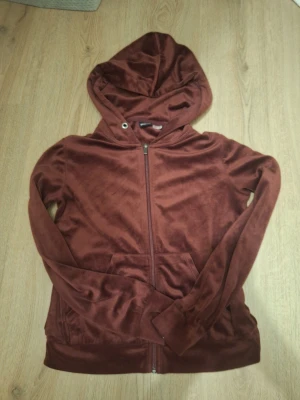 Brun velourhoodie från Gina Tricot - Mysig brun hoodie i mjuk velour från Gina Tricot. Tröjan har dragkedja framtill, huva och fickor på sidorna. Perfekt för chill dagar och har en skön, avslappnad passform. Snygg att matcha med jeans eller mjukisbyxor.