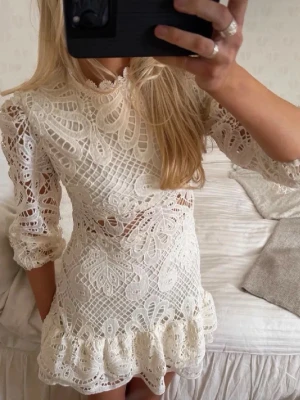 Vit spetsklänning med volang - Säljer en superfin vit kortklänning i spets med volangkant nertill och trekvartsärm. Klänningen har ett detaljerat spetsmönster, hög hals och markerad midja. Perfekt för sommarens alla tillfällen! Lite mindre än vanligt skulle jag säga! mera en S-M