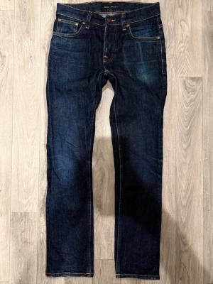 Nudie Jeans Grim Tim Dry Mörkblå W31/L32 - Slim Straight Fit - Nudie Jeans Grim Tim ”Dry True Navy” mörkblå Dry-jeans med slim straight fit-passform, normal midja och raka ben, storlek W31/L32, midja 37,5 cm, ytterbenslängd 102,5 cm, benöppning 17 cm, modellen är 185cm & väger 65kg, i fint skick.