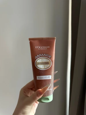 L'Occitane Amande Shower Scrub - L'Occitane Amande Shower Scrub är en exfolierande duschskrubb med krossade mandlar. Tuben är brun med grön kork och har en mjuk, krämig formula som rengör och peelar huden. Perfekt för dig som vill ha len och fräsch hud med en lyxig känsla.