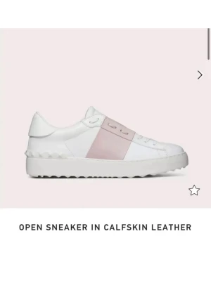Valentino vit och rosa sneaker - Snygga sneakers från Valentino i vitt kalvskinn med en bred ljusrosa rem över mitten. Klassisk låg modell med vita snören och subtila nitar på hälen. Perfekta för dig som vill ha en clean men ändå unik look.