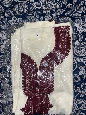 Vit traditionell tunika med vinröd brodyr - Säljer en vit traditionell tunika med detaljerad vinröd brodyr runt halsringningen och framtill. Tunikan har en rak passform och är tillverkad i ett mjukt tyg som känns bekvämt mot huden. Perfekt för dig som gillar unika och stilrena plagg.