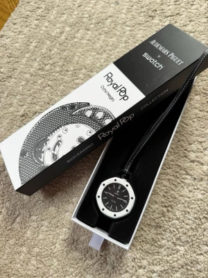 Swatch x Audemars Piguet Royal Pop klocka - Unik Swatch x Audemars Piguet Royal Pop klocka från Bioceramic-kollektionen. Klockan har svart urtavla med vita detaljer och en vit ram, samt svart band med vita sömmar. Snygg och modern design som sticker ut.