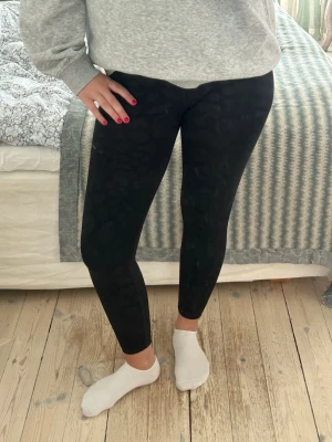 Svarta träningstights - Säljer ett par svarta leggings. De har hög midja och sitter tight längs benen med leopardmönster. Tyvärr har en bit av loggan åkt av men det är inget man märker då de sitter långt ner på benet